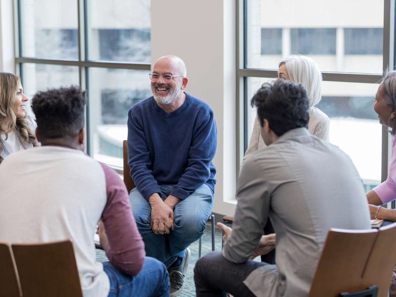 A diverse group of adults sitting together in a supportive circle in a bright community room
